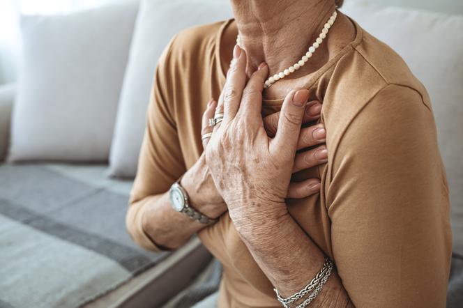 Stan przedzawałowy - starsza kobieta trzymająca sie za klatkę piersiową. 