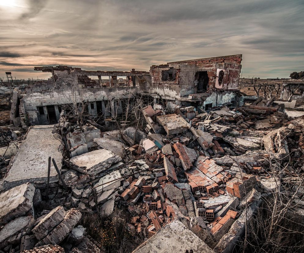 Zrujnowany budynek i gruzy porozrzucane na dużym obszarze pod pochmurnym, szarym niebem, symbolizujące zniszczenia wojenne i zagrożenie dla miast. Więcej o przygotowaniu Polski na kryzysy militarne przeczytasz na Poradnik Zdrowie.
