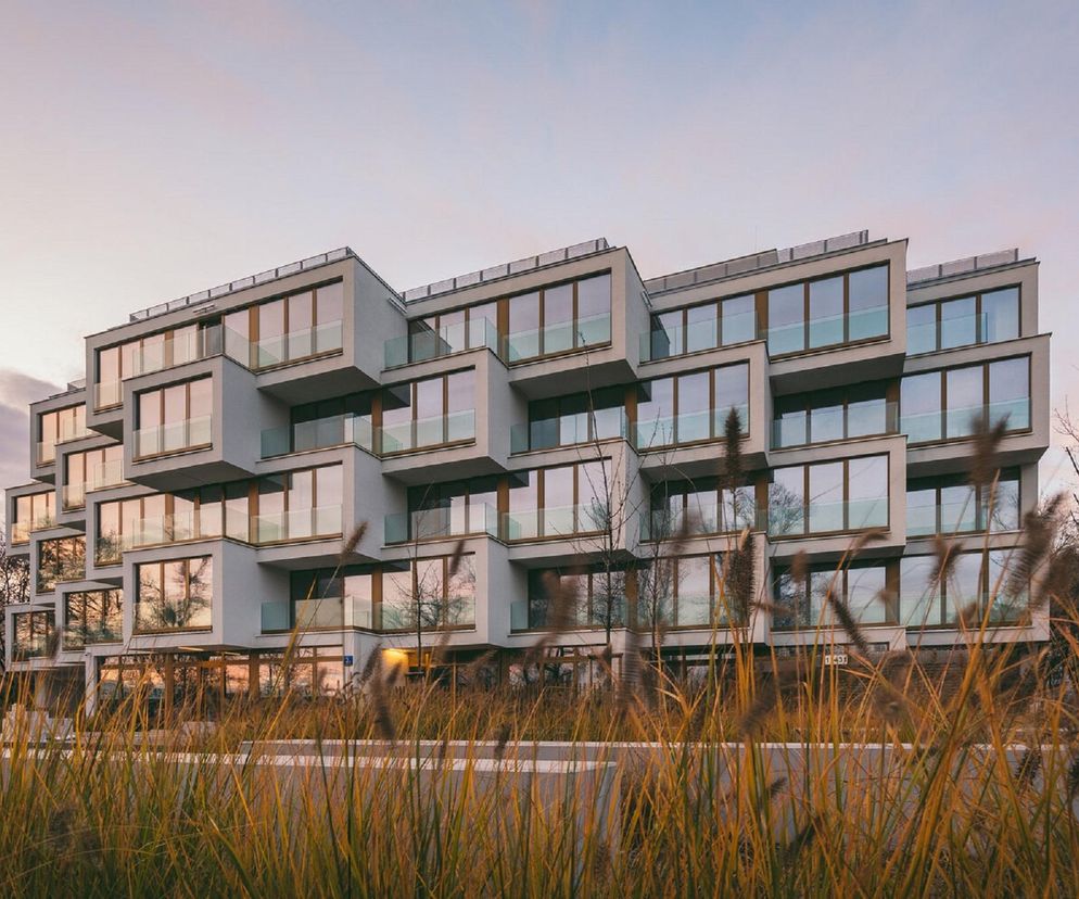 Nowoczesny budynek APARTAMENTY POTOCKA w Warszawie, autorstwa POLE Architekci, z nieregularną bryłą, schodkowymi bokami i licznymi, dużymi oknami, otoczony wysoką trawą. Więcej o tej realizacji i Życiu w Architekturze na Architektura Murator Plus.