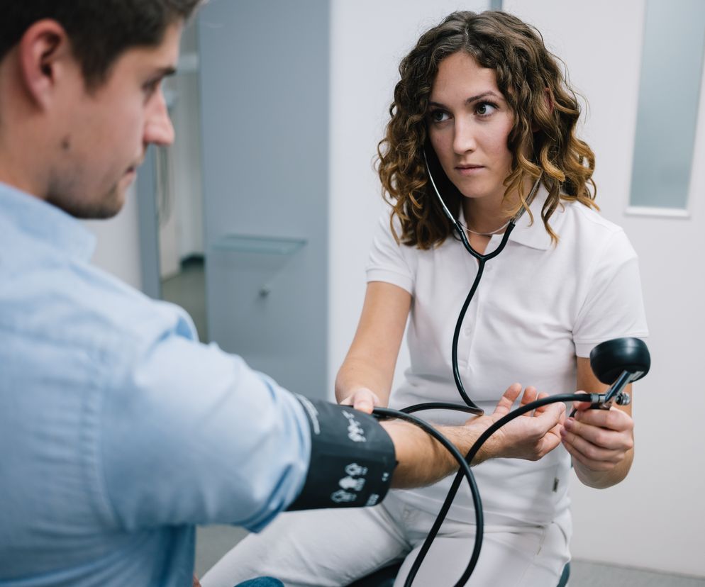 Lekarka mierzy ciśnienie młodemu mężczyźnie w gabinecie lekarskim.