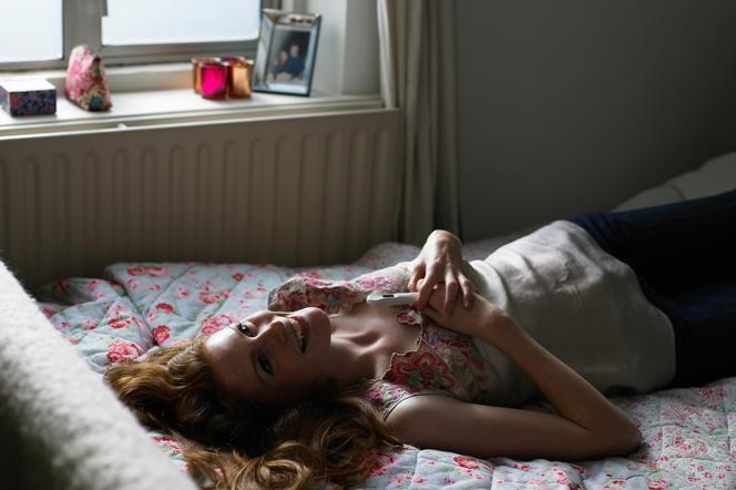Roześmiana kobieta na łóżku z testem w dłoniach 