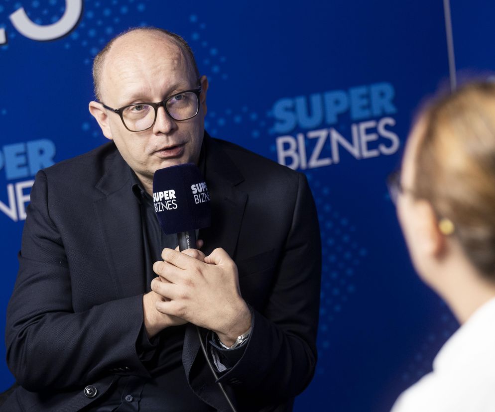 Radosław Nielek, dyrektor NASK, w trakcie wywiadu. Mężczyzna w okularach i ciemnym garniturze trzyma mikrofon z logo Super Biznes.  Zdjęcie ilustruje artykuł na portalu Super Biznes o zagrożeniu blackoutu w Polsce i przygotowaniach do niego.