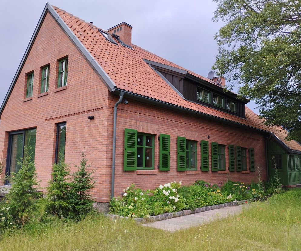 Dom w Szerokim Borze autorstwa Piotra Olszaka, zgłoszony do konkursu Życie w Architekturze 2025, przedstawia tradycyjną elewację z czerwonej cegły i ceramicznym dachem, połączoną z nowoczesnymi elementami. Zielone okiennice i rynny harmonizują z otoczeniem, widocznym na Architektura Murator Plus.