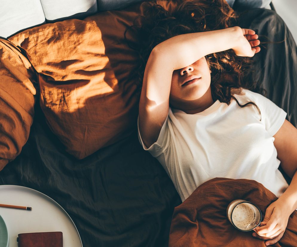 Kobieta leży w łóżku z kubkiem kawy