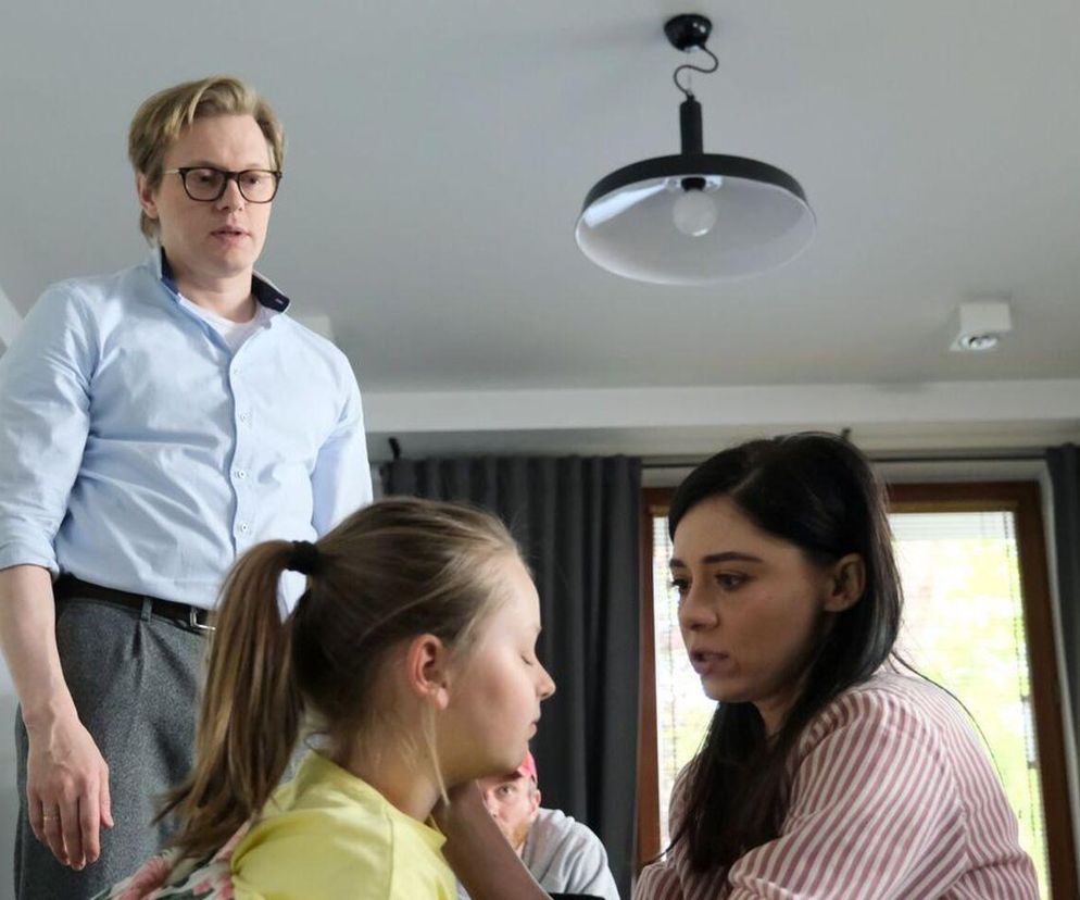 Philippe Tłokiński (Radek) stojący za Adrianą Kalską (Iza) i Laurą Jankowską (Maja) w dramatycznej scenie, gdzie Radek ma uderzyć Maję. Iza rozmawia z córką, podczas gdy Radek obserwuje ich z agresją. Więcej o dramatycznych losach bohaterów przeczytasz na stronie Super Seriale.