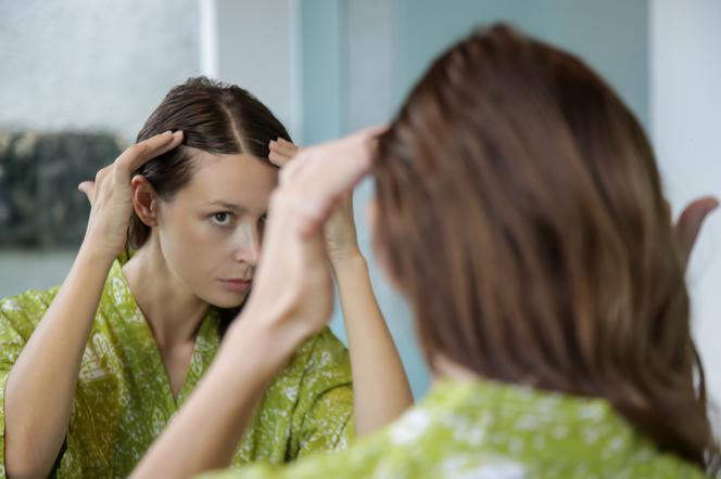 Kobieta ogląda w lustrze swoje włosy