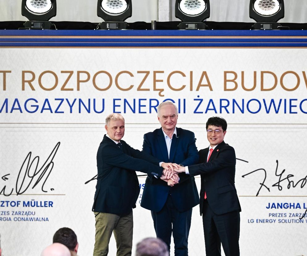 Prezesi: Krzysztof Müller (PGE Energia Odnawialna), Dariusz Marzec (PGE Polska Grupa Energetyczna) i Jangha Lee (LG Energy Solution Wrocław) symbolicznie łączą dłonie na tle napisu Akt rozpoczęcia budowy Magazynu Energii Żarnowiec. O inwestycji przeczytasz na Super Biznes.