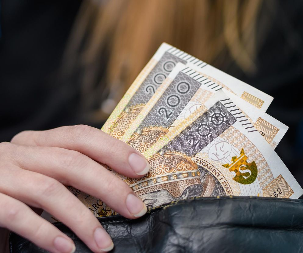 Dłoń kobiety wsuwająca banknoty 200 zł do czarnego portfela, symbolizująca koszty Bezwarunkowego Dochodu Podstawowego (BDP) w Polsce. O skali finansowej i alternatywnych świadczeniach przeczytasz więcej na Super Biznes.