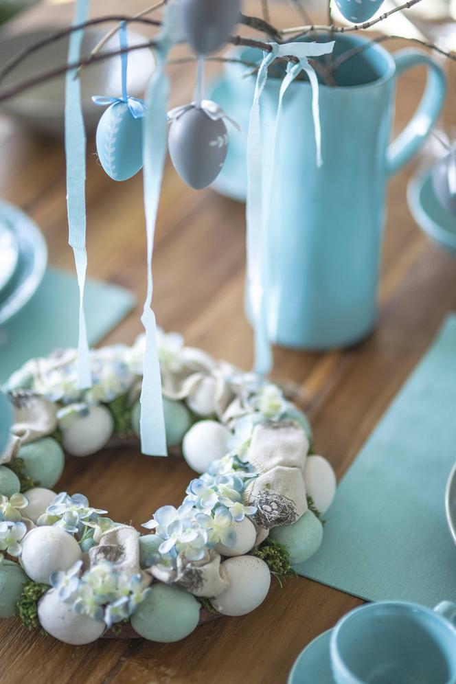 Wianek z wikliny i niebieskich pisanek modna dekoracja stołu na Wielkanoc