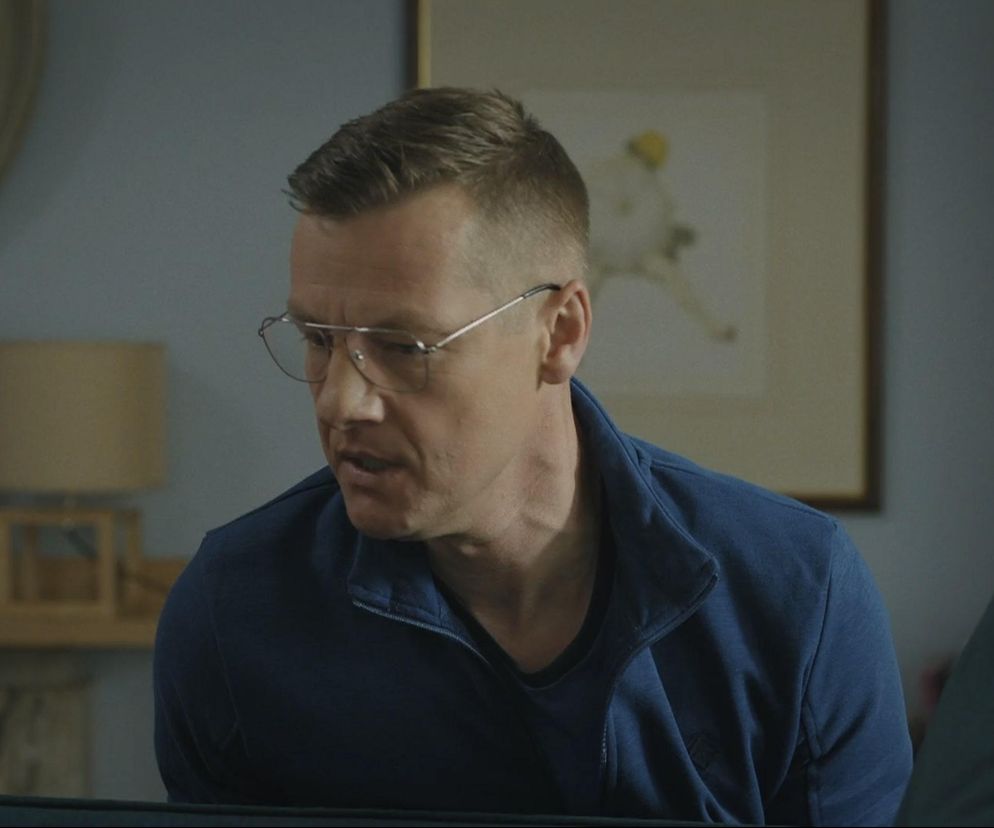 Marcin Mroczek jako Piotrek Zduński w okularach, w granatowej bluzie ze stójką, z zatroskaną miną. Mężczyzna ma krótkie, ciemne włosy. Zduński nie może sobie darować, że zaufał sąsiadowi. Więcej o losach Piotrka przeczytasz na portalu Super Seriale.