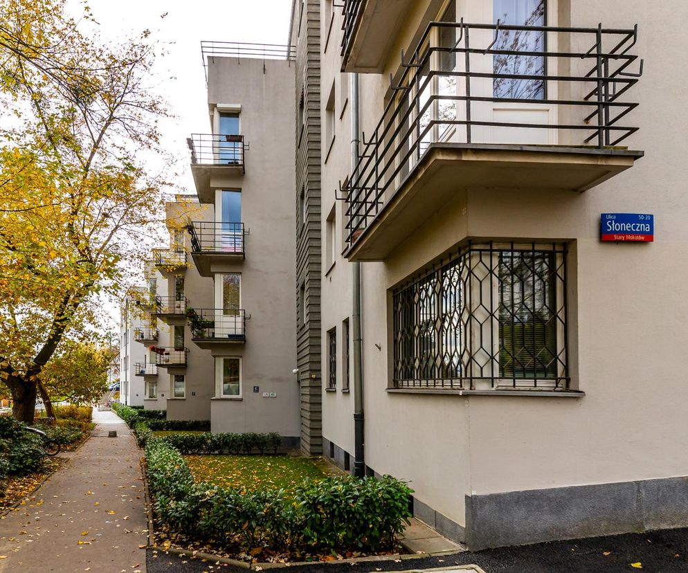 Przedwojenny warszawski blok-harmonijka przy ulicy Słonecznej 50 na Mokotowie, widziany jesienią z perspektywy chodnika. Na zdjęciu widać fasadę z balkonami i zdobionymi kratami okiennymi, oraz tabliczkę z nazwą ulicy. O historii tego miejsca przeczytasz na Architektura Murator Plus.