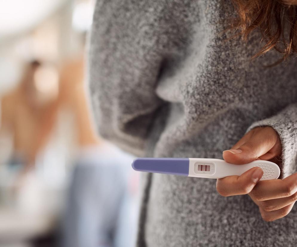 Kobieta z testem ciążowym, który chowa za plecami