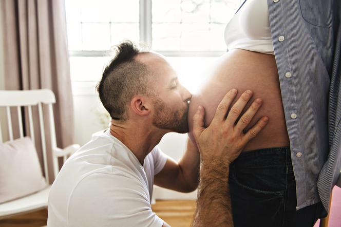 Mężczyzna całuje brzuch żony w ciąży