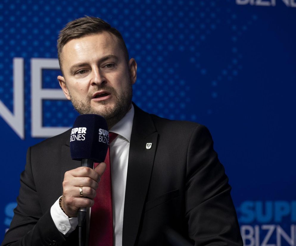 Wicemarszałek Województwa Dolnośląskiego Michał Rado podczas wywiadu, trzymający mikrofon Super Biznes, rozmawia o programach infrastrukturalnych i koalicjach politycznych, co można przeczytać na Super Biznes.