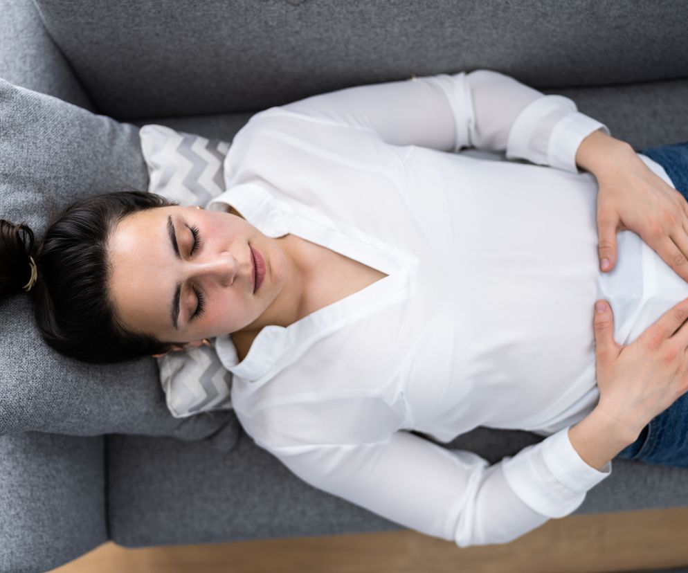 Zbliżenie na kobietę, która leży na sofie i trzyma ręce na brzuchu