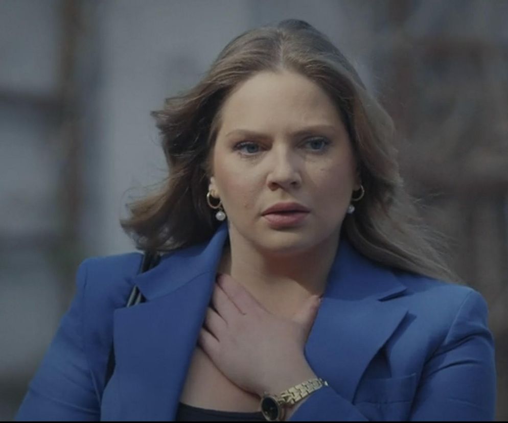 Melania Grzesiewicz jako Anita w „M jak miłość” z zaniepokojeniem patrzy w dal, dotykając dłonią klatki piersiowej, ubrana w granatową marynarkę. Scena dotyczy podejrzeń o zdradę Kamila, o której przeczytasz więcej na Super Seriale.