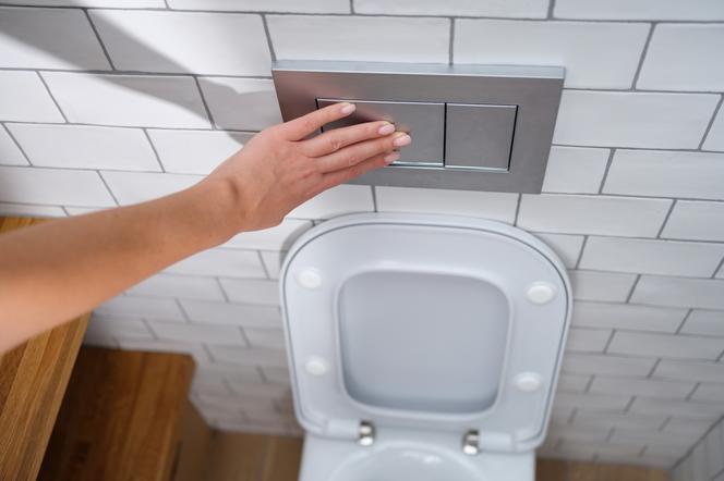 Zbliżenie na dłoń kobiety na przycisku spłukiwania toalety 