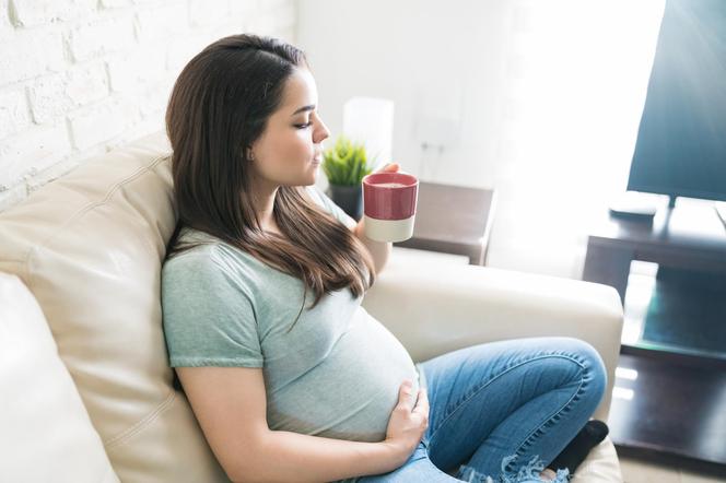 Kobieta w ciąży na kanapie pije herbatę