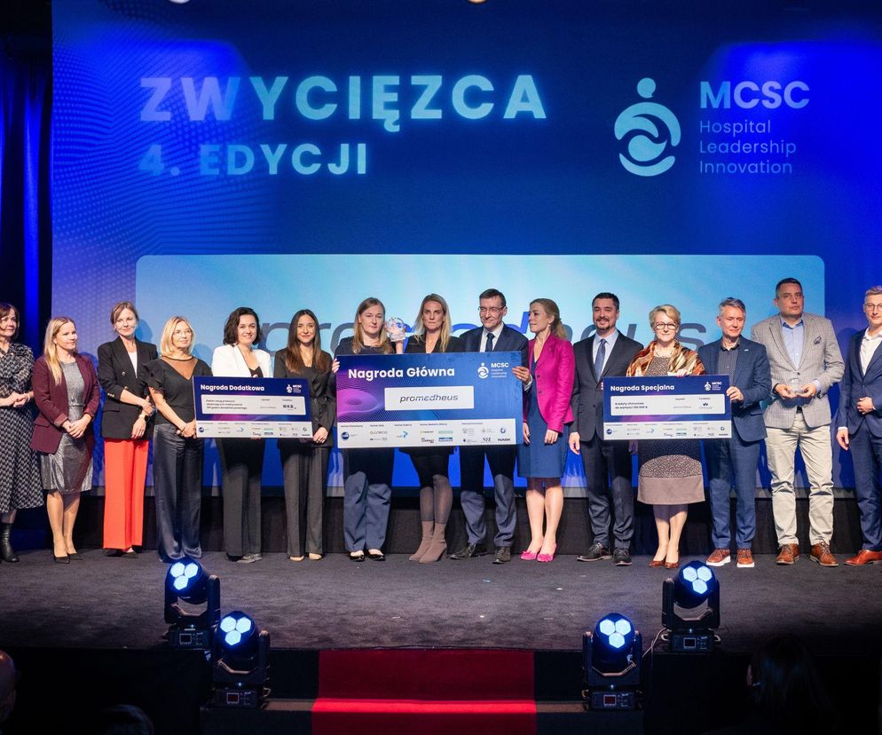 Grupa uczestników gali finałowej MCSC Hospital Leadership Innovation pozuje na scenie z nagrodami, m.in. z czekiem dla zwycięzcy 4. edycji, systemu Promedheus. Możesz przeczytać o innowacjach w medycynie na portalu Poradnik Zdrowie.