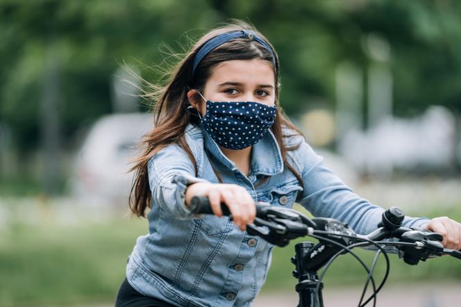 Dziewczynka jadąca na rowerze w maseczce na twarzy