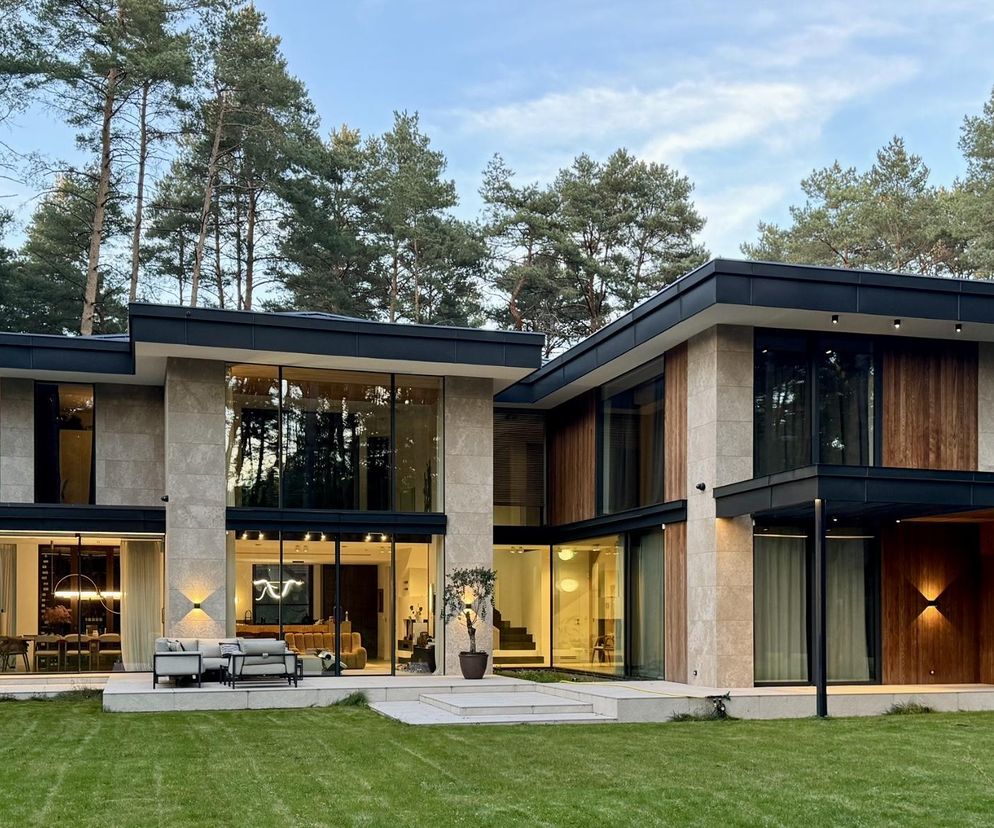 Nowoczesna rezydencja w lesie projektu MAG Architekci, z dużymi przeszkleniami i elementami drewnianymi, otoczona wysokimi sosnami. Architektura Murator Plus to miejsce, gdzie znajdziesz więcej o takich innowacyjnych projektach.