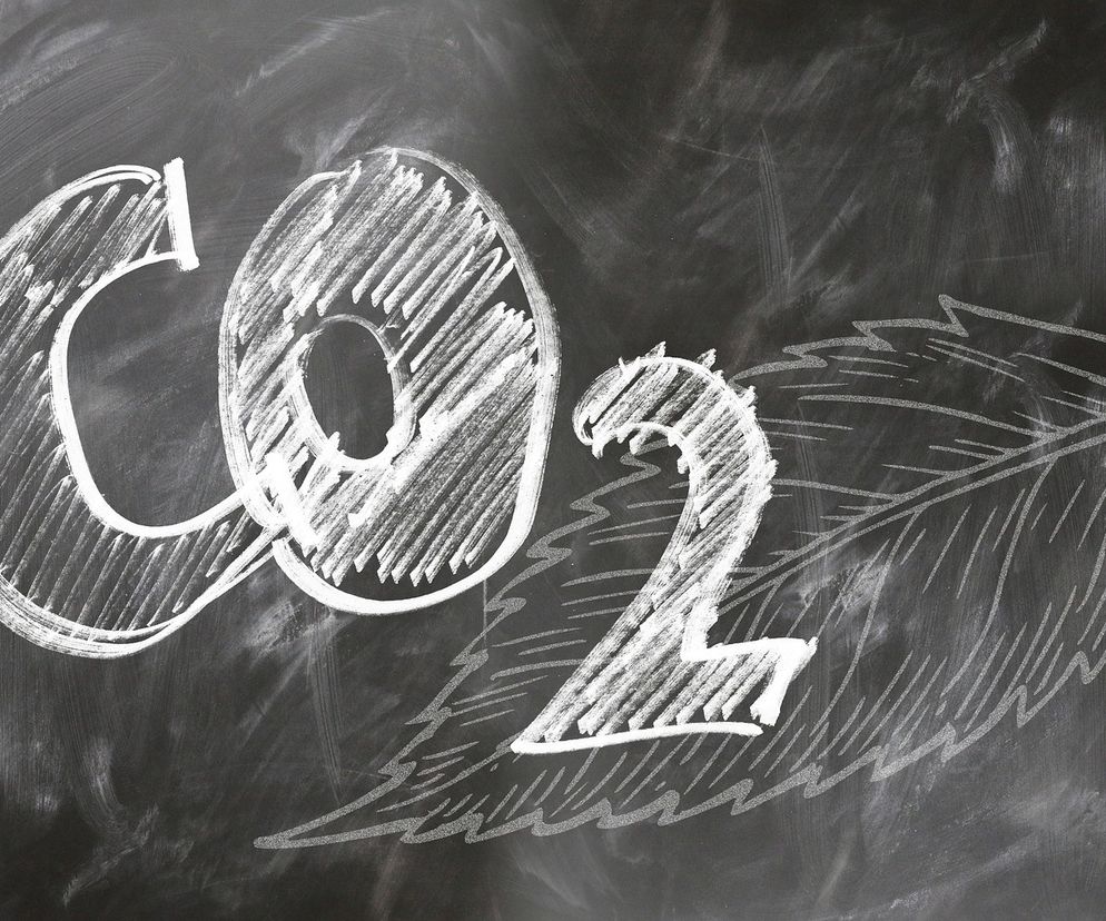 Napis CO2 narysowany kredą na tle czarnej tablicy, symbolizujący emisje dwutlenku węgla i unijną politykę klimatyczną. W tle liść, również narysowany kredą. Wskazuje to na wyzwania związane z ETS2, o których przeczytasz na Super Biznes.
