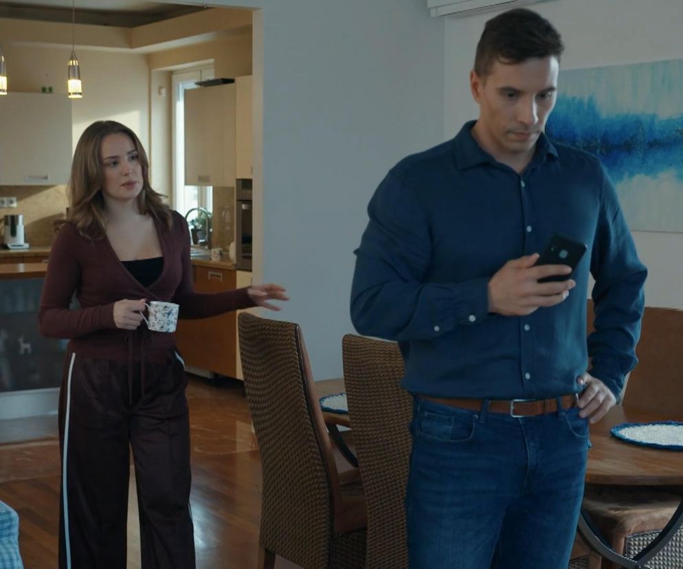 Wiktoria Gąsiewska jako Oliwka z kubkiem, z dłońmi wyciągniętymi w stronę Tomasza Kępskiego (Jakub Sokołowski), który odwraca wzrok, patrząc w ekran telefonu, ignorując ją, siedząc przy okrągłym stole. Kuchnia w tle. Scena z serialu „Barwy Szczęścia” dostępnego na Super Seriale.