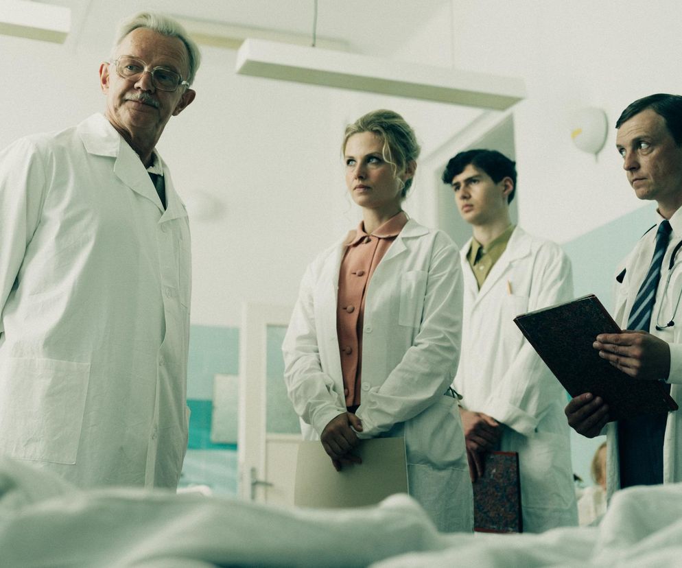Grupa lekarzy w białych fartuchach w szpitalu z lat 60. Cztery osoby, dwie kobiety i dwóch mężczyzn, stoją obok łóżka pacjenta. Zdjęcie przedstawia scenę z serialu „Czarna śmierć” o epidemii ospy we Wrocławiu. Więcej o nowościach ze świata Super Seriale znajdziesz na naszym portalu.