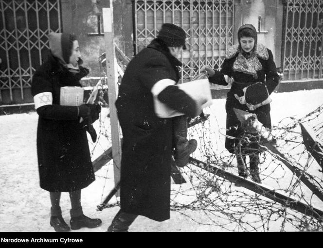 Troje Żydów przechodzi przez zasieki z drutów kolczastych w getcie, 1942.