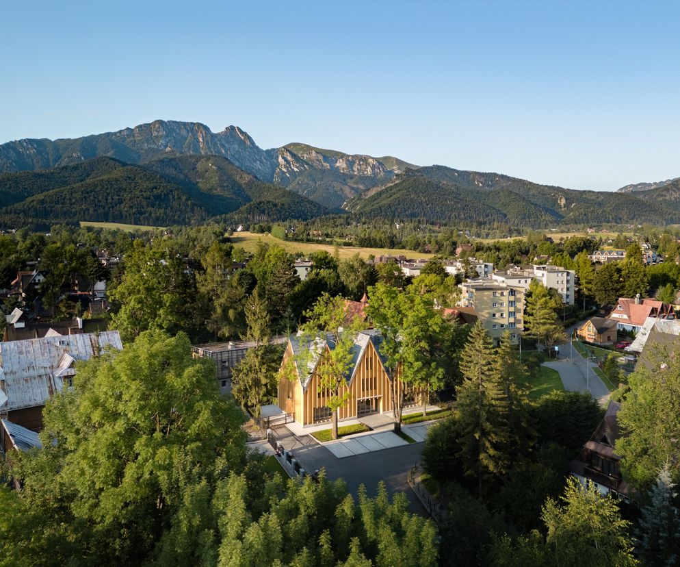 Nowoczesny budynek Centrum Wsparcia Rodzin Nasz Dom w Zakopanem, otoczony zielenią, z drewnianą elewacją i spadzistym dachem, wpisuje się w krajobraz Podhala. W tle widoczne Tatry. Więcej o architekturze regionalnej na Architektura Murator Plus.