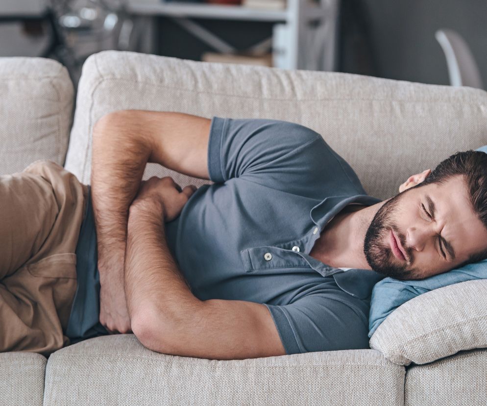 Mężczyzna leży na kanapie z silnym bólem brzucha