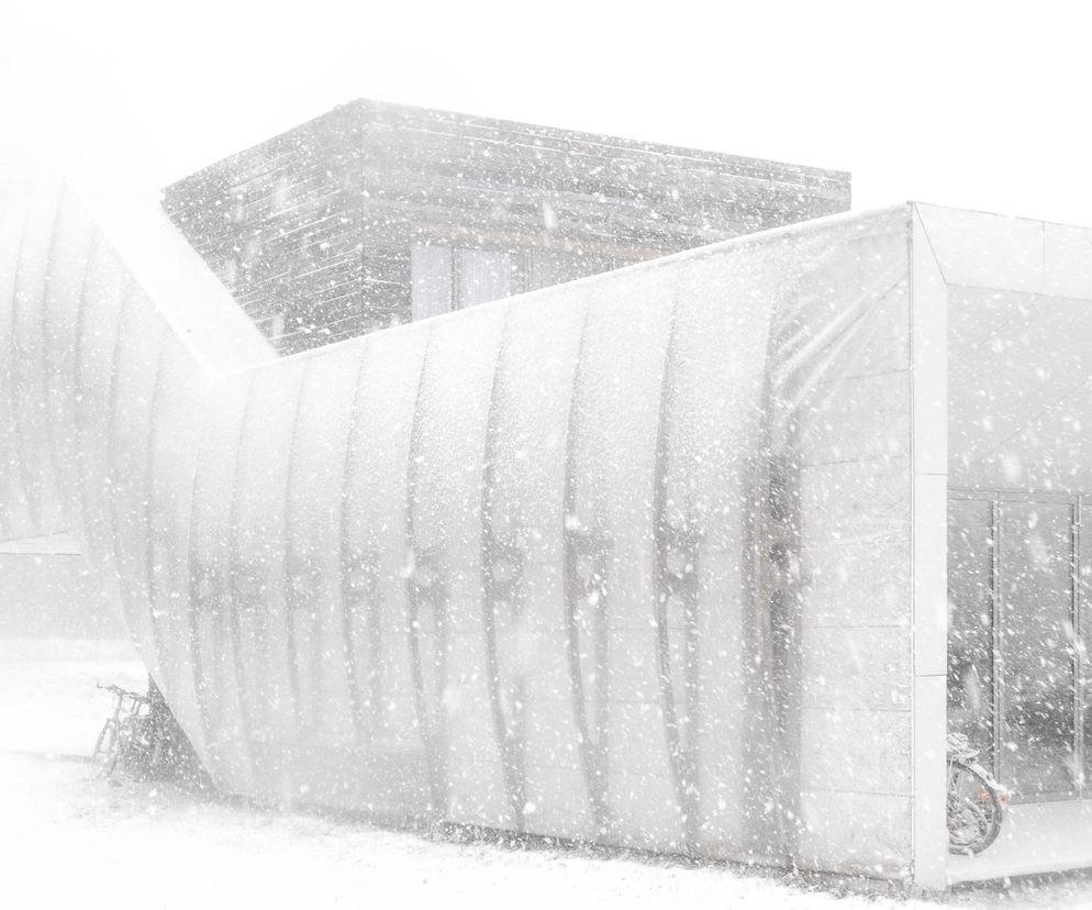 Dom Robak autorstwa Piotra Kuczia w Zabłociu, pokryty śniegiem. Nowoczesna architektura domu jednorodzinnego o białej, zakrzywionej fasadzie i dużych przeszkleniach. Projekt podkreśla relację z naturą, co docenia Architektura Murator Plus.