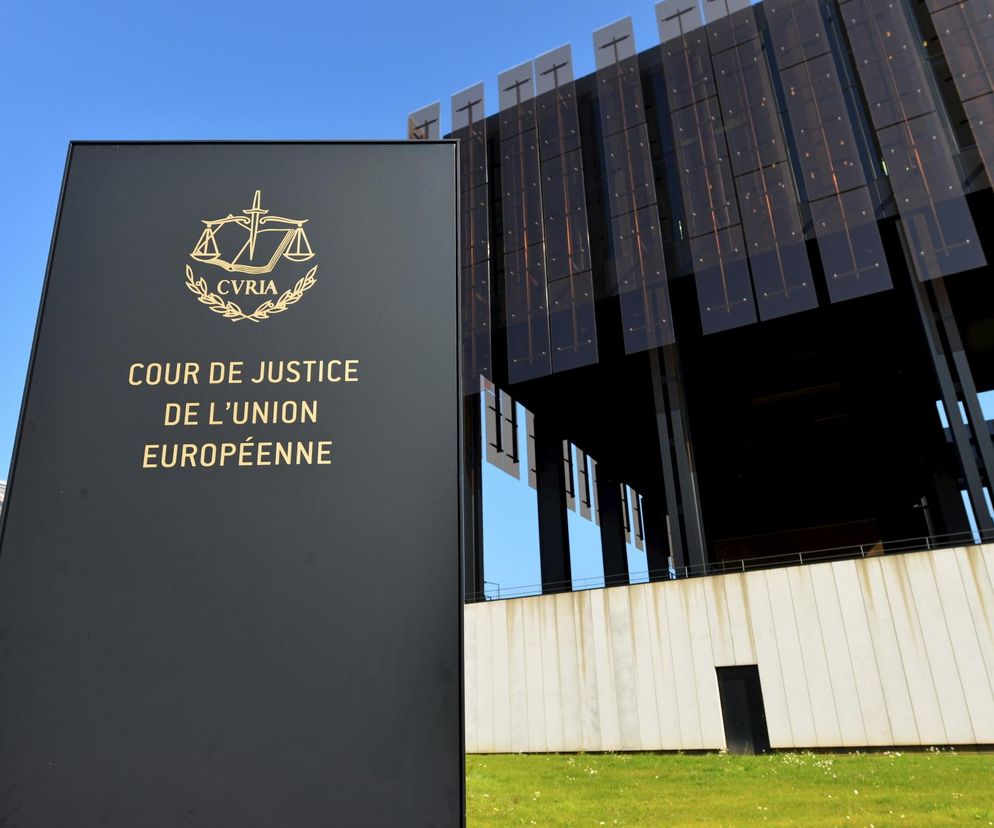 Tablica z napisem Cour de Justice de l'Union Européenne i symbolem wagi, stojąca przed nowoczesnym budynkiem TSUE w Brukseli. Zdjęcie ilustruje pozew Komisji Europejskiej przeciwko Polsce o brak aktualizacji planu klimatycznego, o czym więcej przeczytasz na Super Biznes.