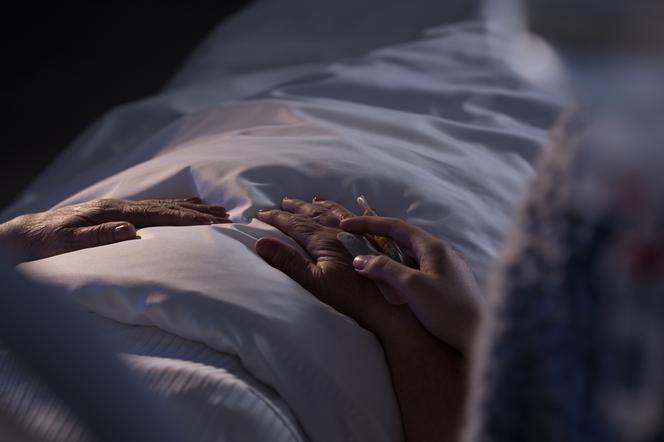 zbliżenie na dłonie osoby leżącej na szpitalnym łóżku i jej gościa