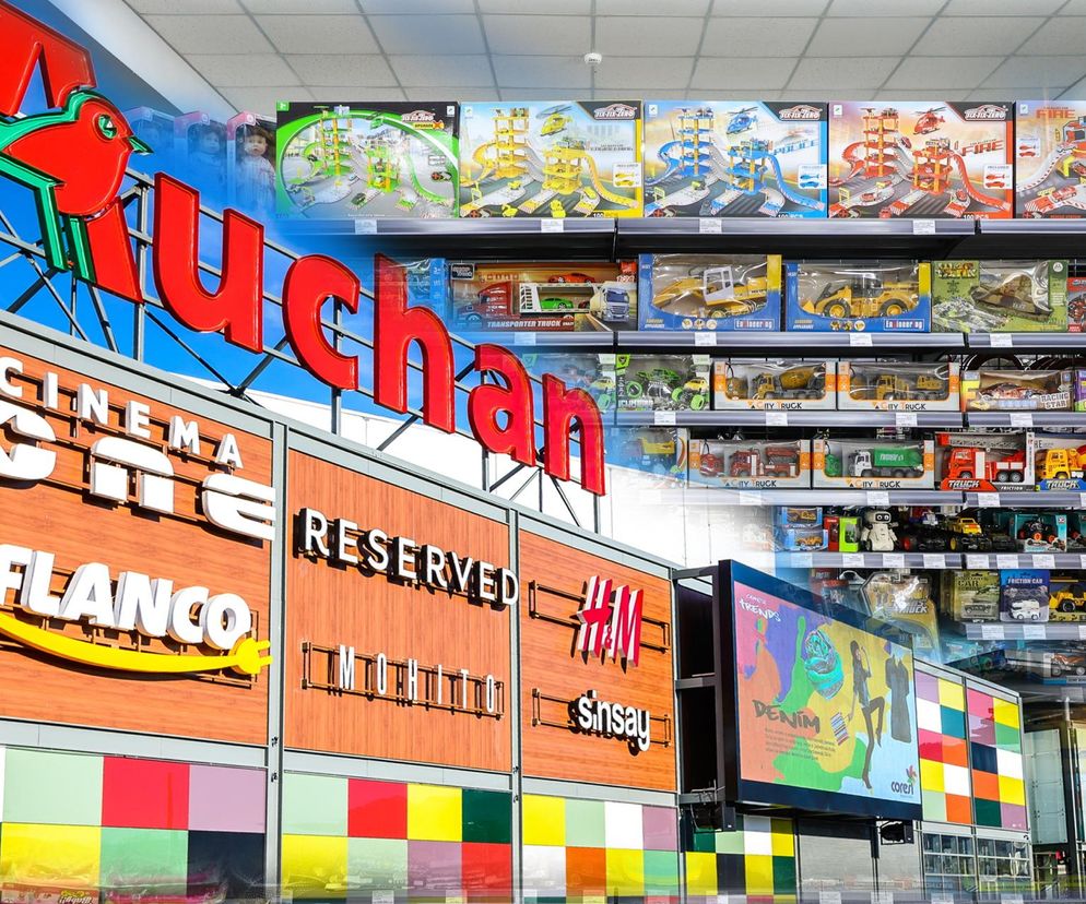 Zdjęcie przedstawia półki sklepowe Auchan wypełnione zabawkami, głównie samochodzikami. Widoczne są także inne sklepy w galerii handlowej.  To ilustracja artykułu na Super Biznes o szaleństwie wokół promocji Hot Wheels w Auchan, gdzie klienci walczyli o zabawki.  Szczegółowo pokazano zróżnicowany asortyment zabawek, co podkreśla skalę promocji opisanej na portalu Super Biznes.