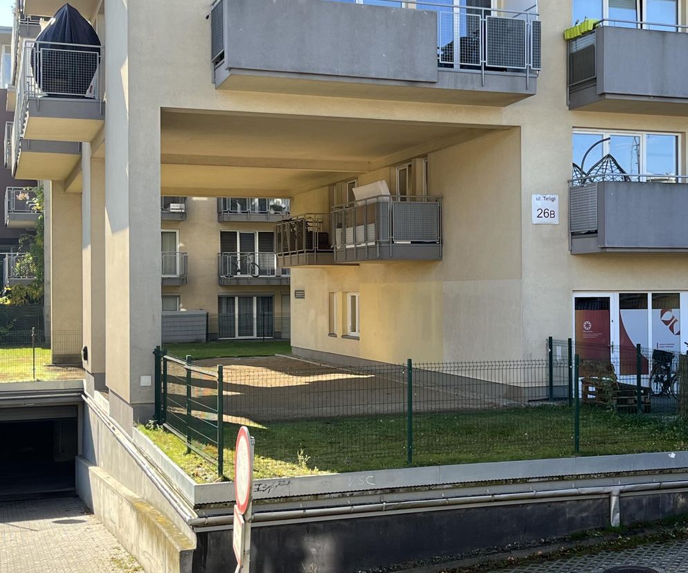 Blok mieszkalny przy ulicy Teligi 26B w Krakowie z charakterystycznymi balkonami schowanymi we wnęce budynku, z zielonym ogrodzeniem i wjazdem do garażu podziemnego. Więcej o nietypowej architekturze Krakowa przeczytasz na Architektura Murator Plus.