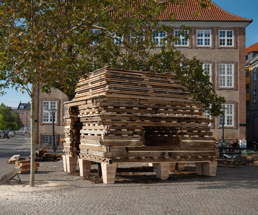 Pawilon Barn Again Toma Svilansa i studia THISS, zbudowany z odzyskanych drewnianych elementów konstrukcyjnych, stoi na brukowanym placu Gammel Strand w Kopenhadze. Projekt ten redefiniuje architekturę w duchu „Slow Down”, co można przeczytać na Architektura Murator Plus.