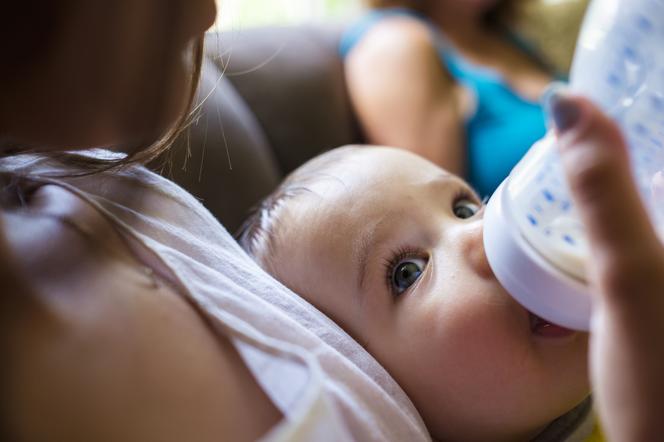 niemowlę w ramionach mamy pijące mleko z butelki