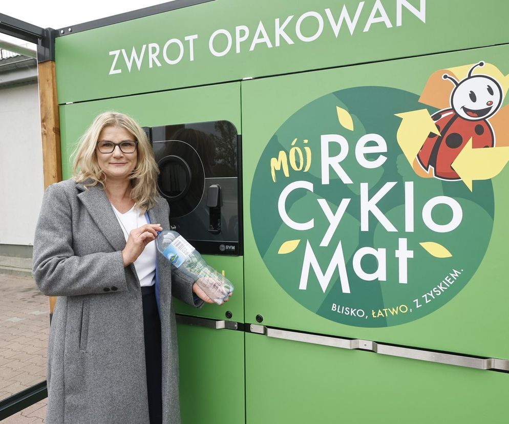 Agnieszka Koc, Dyrektorka Ochrony Środowiska i Zrównoważonego Rozwoju w sieci Biedronka, prezentuje zasady korzystania z recyklomatu, trzymając plastikową butelkę. Zielony automat z napisem Mój Recyklo Mat i grafiką uśmiechniętej biedronki w znaku recyklingu symbolizuje ekologiczne rozwiązania systemu kaucyjnego. Więcej o tym przeczytasz na Super Biznes.