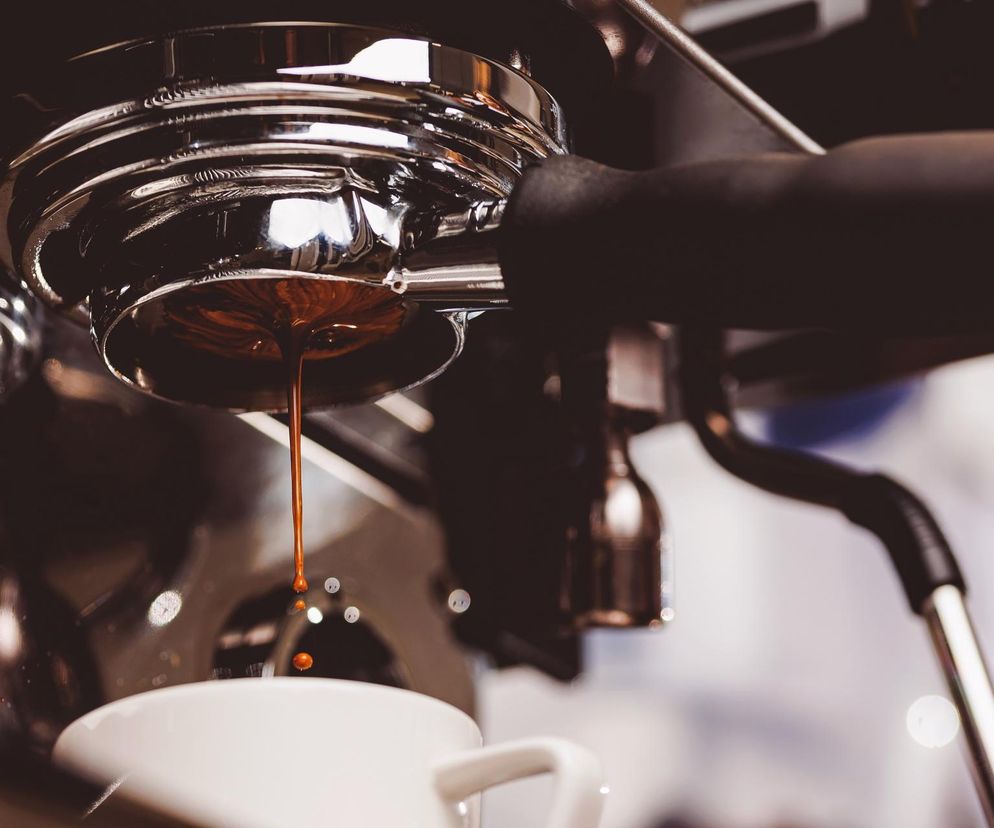 Ekspres ciśnieniowy przygotowujący kawę, z której w kubku tworzy się ciemne, aromatyczne espresso. Scena symbolizuje codzienny wydatek, jakim jest zakup kawy, co nawiązuje do analizy rankomat.pl o sile nabywczej Polaków, o której można przeczytać na Super Biznes.
