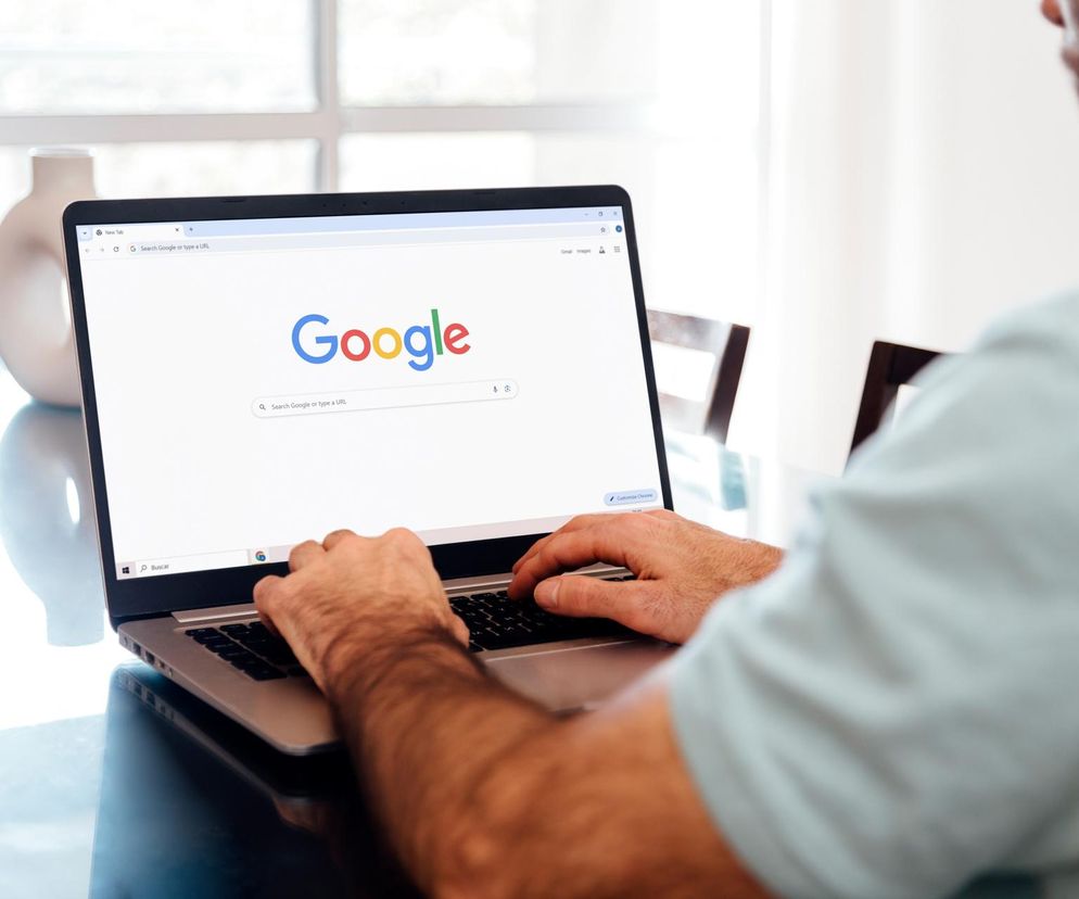 Ręce mężczyzny piszącego na laptopie, na którego ekranie wyświetla się strona główna wyszukiwarki Google. Obraz symbolizuje dominującą pozycję Google na rynku cyfrowym i kwestie regulacji antymonopolowych, o których szerzej przeczytasz na portalu Super Biznes.