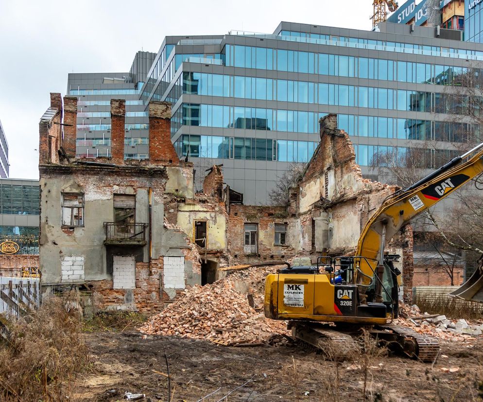 Koparka burzy starą, ceglaną kamienicę na tle nowoczesnych szklanych biurowców. O niszczeniu zabytków przeczytasz na Architektura.