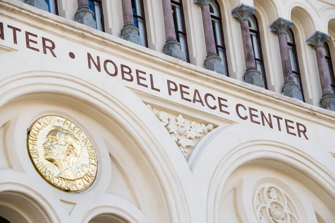 Zewnętrzna fasada budynku Nobel Peace Center w Oslo z jasnymi ścianami, brązowymi napisami NOBEL PEACE CENTER i złotą plakietką z profilem Alfreda Nobla. Na Poradnik Zdrowie znajdziesz informacje o Nagrodzie Nobla z medycyny.