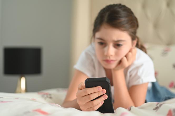 dziewczynkależąca na łóżku z telefonem w dłoni