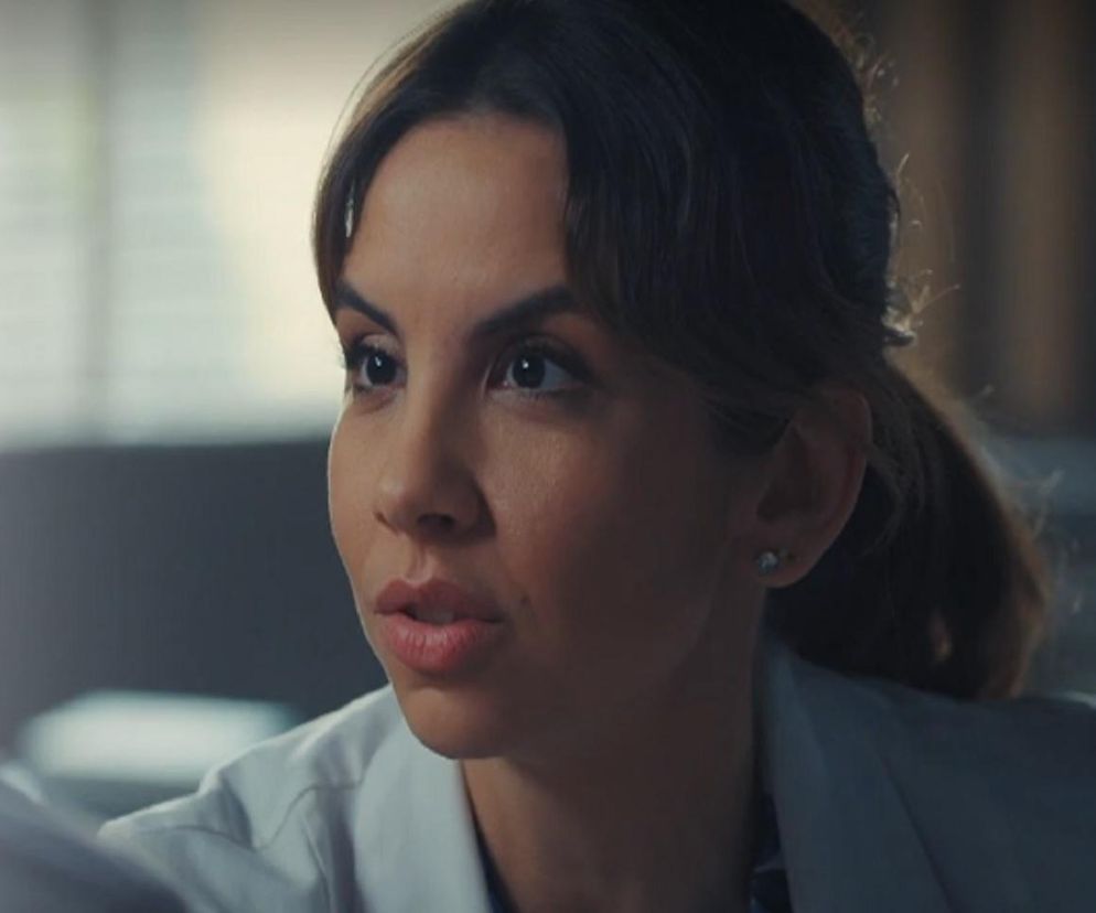 Ilona Janyst jako Aneta Chodakowska w serialu M jak miłość. Aneta z poważnym wyrazem twarzy, częściowo odwrócona, patrzy na rozmówcę. Kobieta ma związane włosy, kolczyki sztyfty i biały kitel, co świadczy o jej zawodzie lekarza. Artykuły o serialu znajdziesz na Super Seriale.