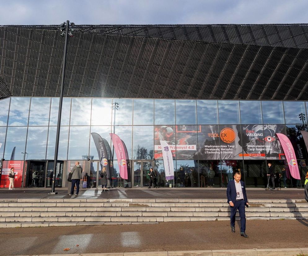 Międzynarodowe Centrum Kongresowe w Katowicach, widok na nowoczesny budynek z dużymi, przeszklonymi drzwiami, przed którymi stoi grupa osób i bannery reklamowe imprez branżowych, takich jak TOOLEX i ExpoWELDING. O konferencji Przemysł dla obronności przeczytasz na Super Biznes.