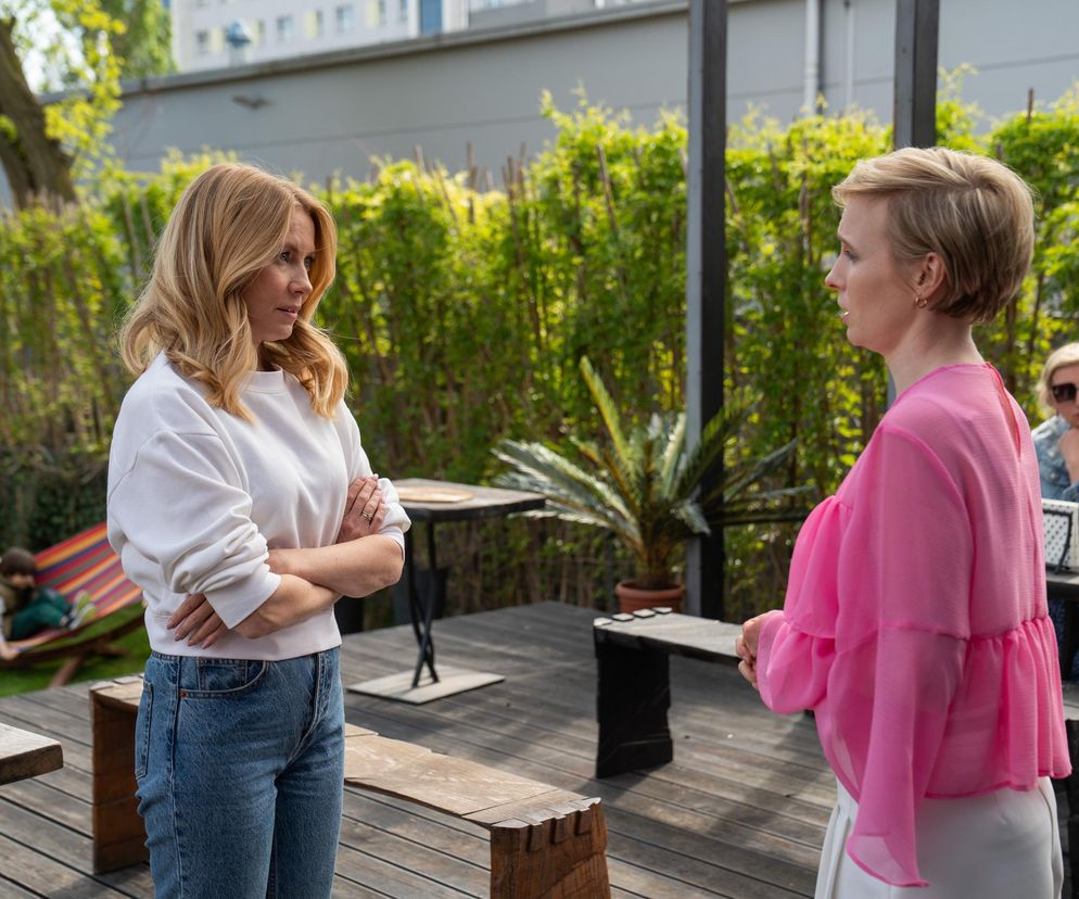 Dominika (Karolina Chapko) w białej bluzie i jeansach z założonymi rękami patrzy na Sonię (Weronika Nockowska) w różowej bluzce, która opowiada jej o Stefaniaku. W tle Mateuszek w hamaku i Sonia Stefaniak, o której więcej przeczytasz na portalu Super Seriale.