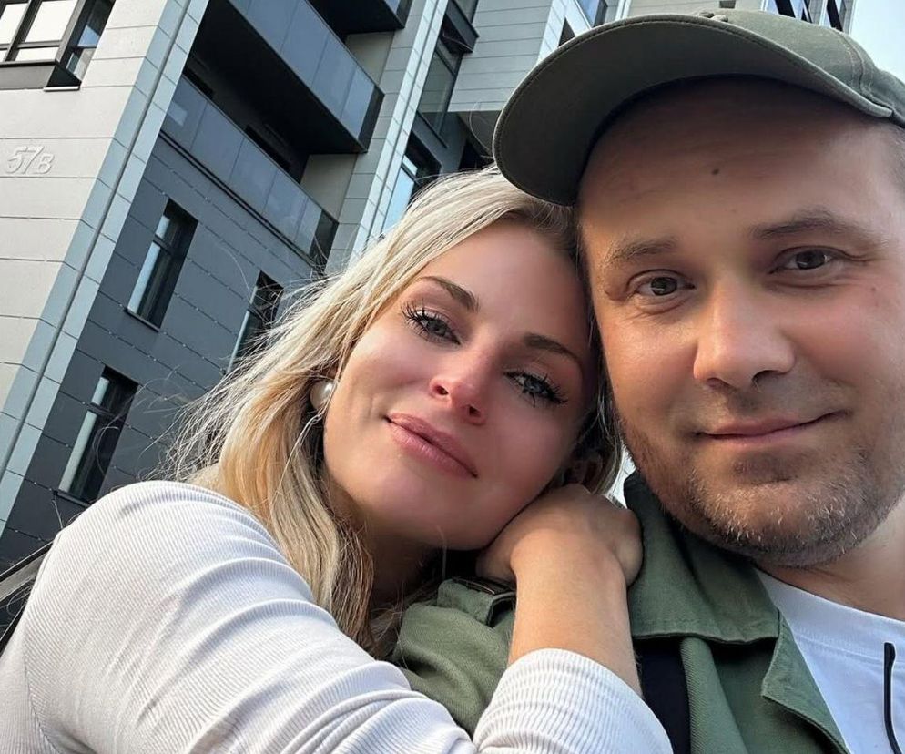 Blondwłosa Anita i Adrian z programu Ślub od pierwszego wejrzenia pozują na tle budynku. Kobieta opiera głowę na ramieniu męża, który zmaga się z glejakiem IV stopnia. Anita prosi fanów o wsparcie w walce z chorobą, o czym przeczytasz na Poradnik Zdrowie.