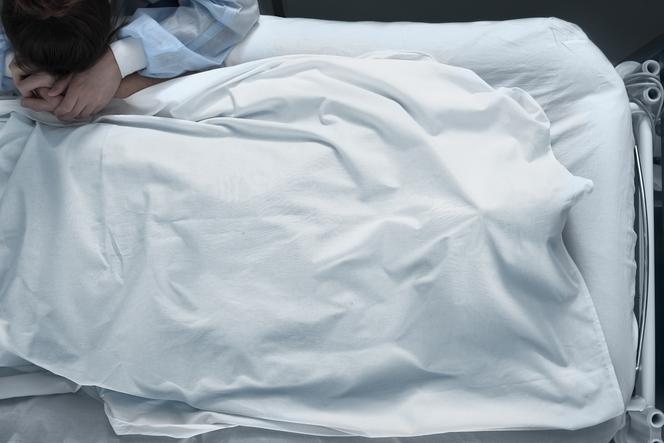 zbliżenie na szpitalne łóżko, nad którym pochyla się kobieta