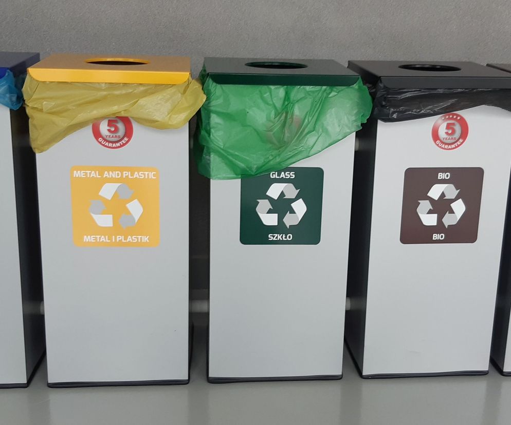 Rząd pięciu pojemników do segregacji śmieci, oznaczonych kolorami i napisami: papier (niebieski), metal i plastik (żółty), szkło (zielony), bio (brązowy), odpady zmieszane (czarny), symbolizujących konieczność segregacji odpadów, o której przeczytasz więcej na Super Biznes.